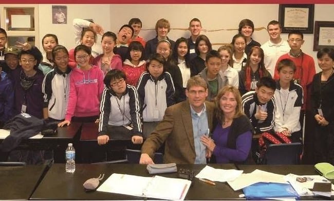 A large group of students gathered around two teachers in a classroom.