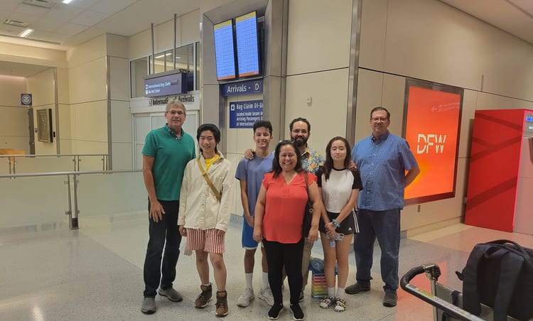 A group of students and host families gathered in an airport arrivals hall.