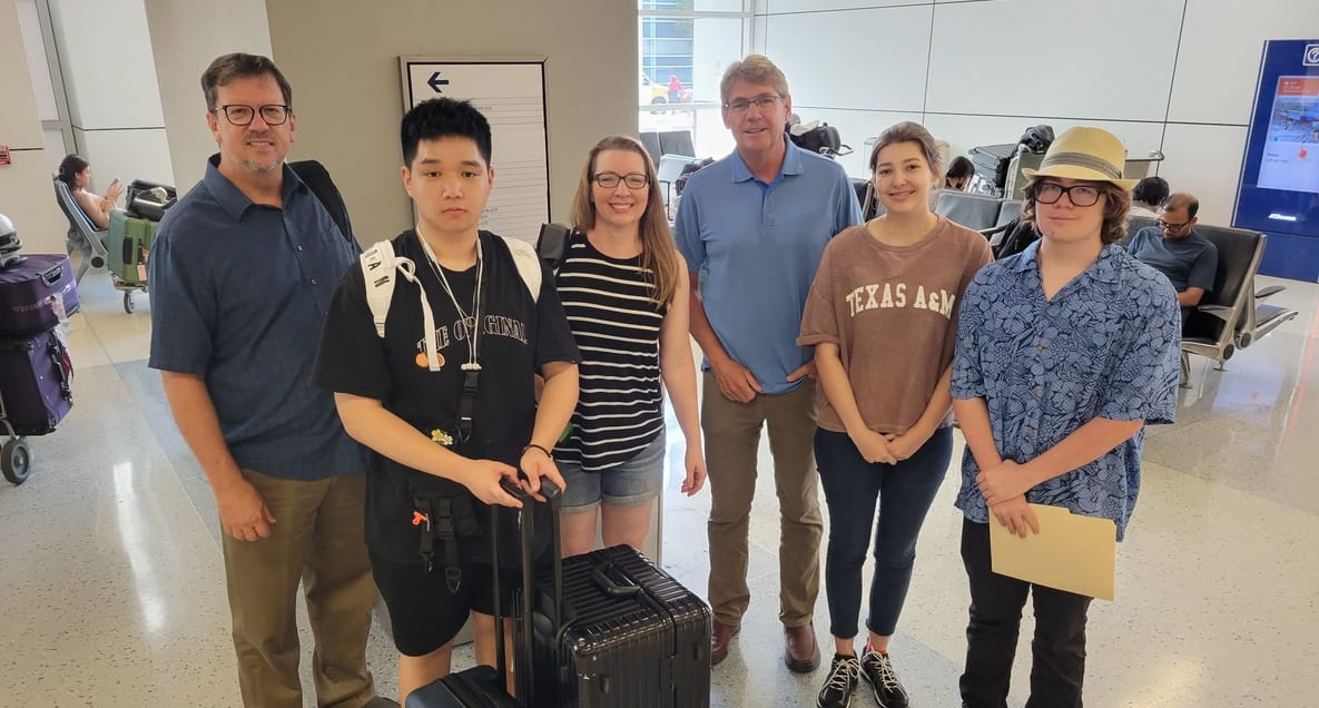 Students and adults standing together with luggage at an airport arrivals hall.